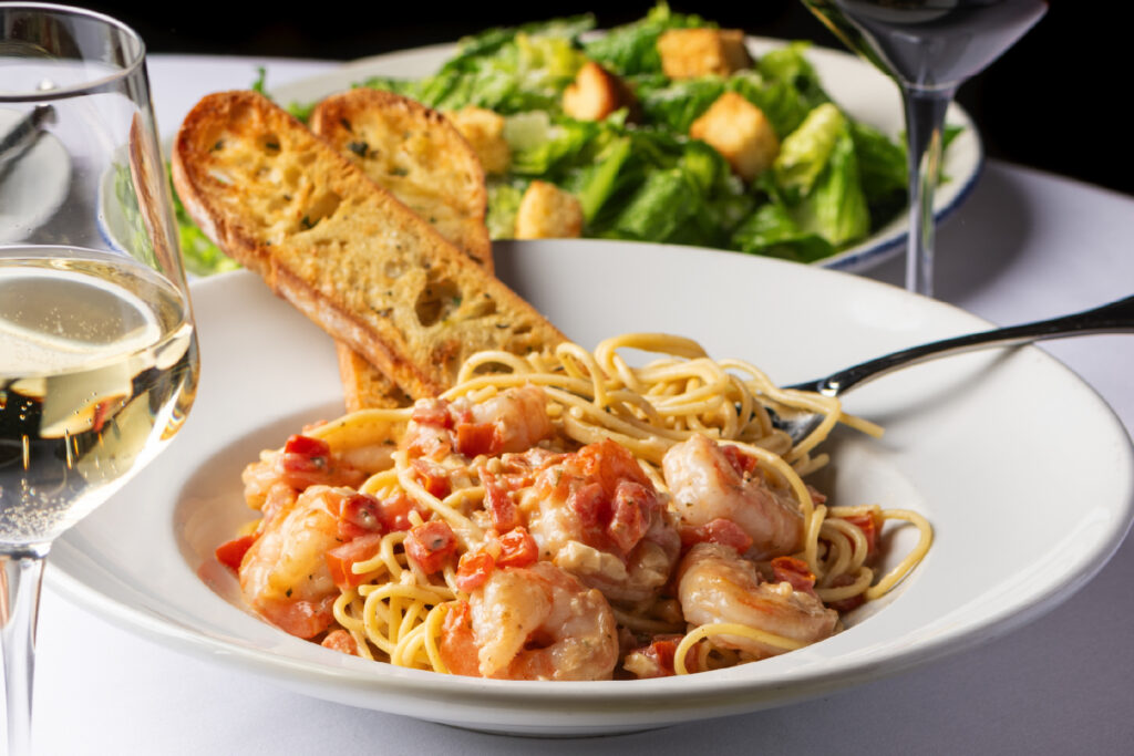 Shrimp Scampi on a plate with a crusty bread and a plate of salad beside it.